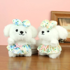 Pair of plush white puppy keychains wearing floral dresses on a warm wooden surface