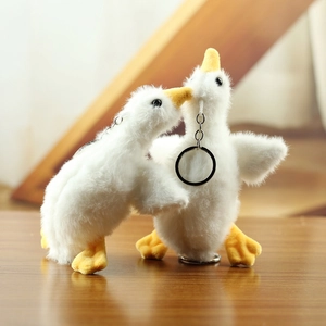 Macro shot of two soft plush goose keychains with yellow beaks on a wooden table