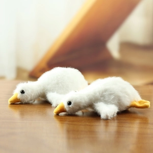 Close-up of two soft white plush goose charms with fluffy texture on a wooden desk