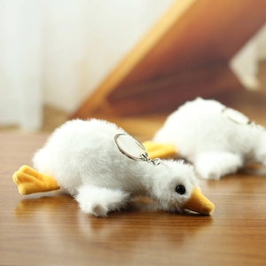 Close-up of cute white plush goose keychain with soft fur and metal ring on wooden table
