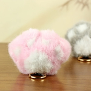 Détail d'un porte-clés patte de chat en peluche rose et blanc avec anneau doré sur bois