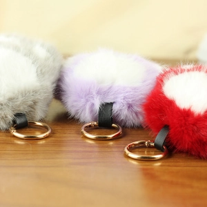 Gros plan de porte-clés patte de chat en peluche grise, violette et rouge avec anneaux dorés