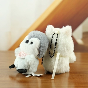 Detailed view of plush penguin and cat keychain charms on a warm wooden background
