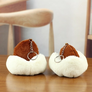 Close-up of two plush hat-shaped keychains with white and brown faux fur on wood