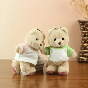 Plush teddy bear keychains in pink and green shirts on a rustic wooden table