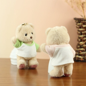 Close-up of plush teddy bear keychains in green and pink tees on a wooden table