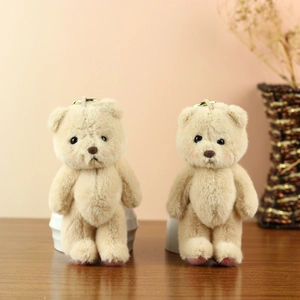 Close-up of two beige plush teddy bear keychains with golden rings on wooden surface