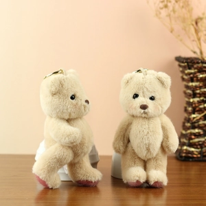 Detail of beige plush teddy bear keychains with gold metal rings on a wooden table