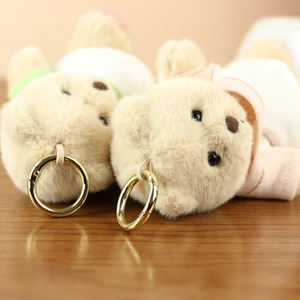 Close-up of beige plush teddy bear keychains with golden metal rings on wood