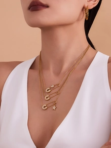 Dettaglio di una collana a strati in oro con ciondoli a graffetta e stella su una modella