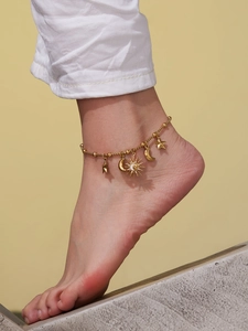 Détail d'une chevillère dorée avec pendentifs soleil, lune et étoiles sur le pied d'un modèle