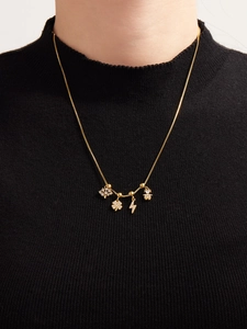Dettaglio di una collana dorata con pendenti in zircone lucente, trifoglio e icone a fulmine