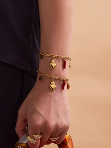 Close-up of golden bracelets with heart and red chili pendants worn by a model