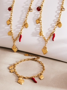 Detail view of gold stainless steel necklace with chili and heart charms on white stand