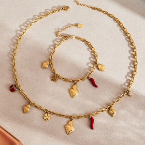 Stainless steel jewelry set with heart, red pepper, and clover charms on a warm background