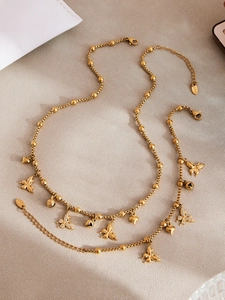 Detailweergave van vergulde vlinder- en hartbedels aan de roestvrijstalen kralenketting