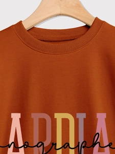 Close-up of the ribbed neckline and graphic lettering on a terracotta long sleeve sweatshirt