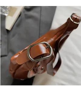Detail of adjustable wide leather shoulder strap with vintage metal buckle on brown bag