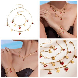 Dettaglio macro di ciondoli a fragola e ciliegia placcati oro 18k su set di gioielli in acciaio
