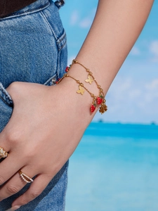 Dettaglio di un bracciale con ciondoli a fragola e farfalla placcato in oro 18k in spiaggia