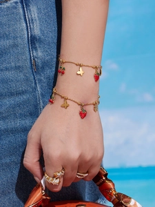 Dettaglio di bracciali e anelli placcati in oro con ciondoli in smalto a forma di frutta