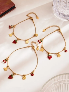 Dettaglio di bracciali in acciaio dorato con ciondoli smaltati a fragola e ciliegia