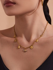 Detail van gouden ketting met bijen- en madeliefjesbedels gedragen door een model