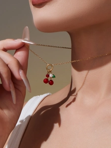 Detail van een gouden kersenketting met rode kralen en een parel op de nek van een model