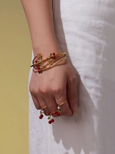 Detailweergave van rode kersenhangers aan gouden armbanden en parelringen aan de pols