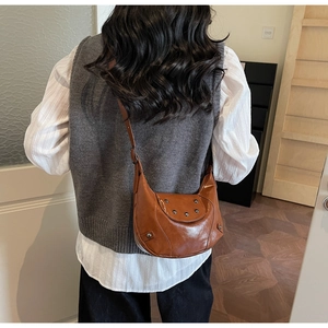 Détail du sac bandoulière en demi-lune marron caramel avec rivets argentés et texture en simili-cuir