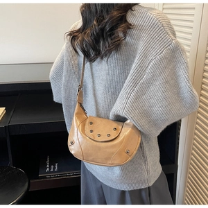 Détail du sac dumpling en cuir camel avec clous métalliques porté par un mannequin