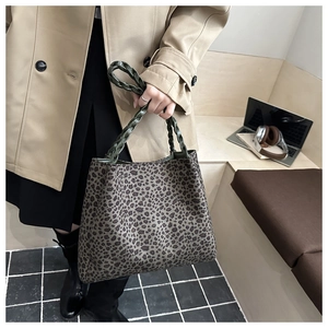 Detail of leopard print tote bag featuring green woven leather handles and large capacity