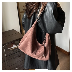 Detail of brown suede hobo bag with braided strap and tassel zipper on black leather jacket