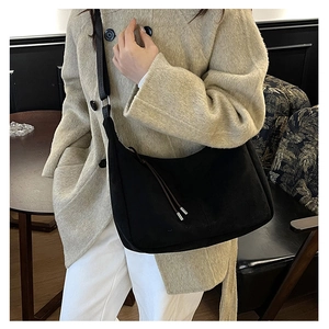 Detail of black suede hobo bag with drawstring accents worn over a beige winter coat
