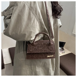 Détail du sac bandoulière léopard en daim avec logo doré porté sur un manteau