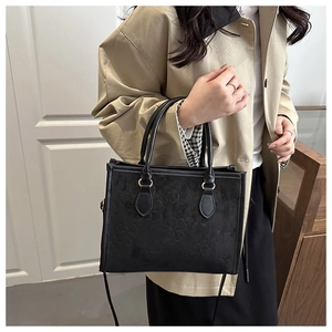 Detail of black faux leather handbag with embossed clover patterns and twin handles