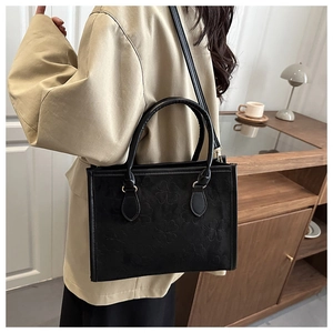 Detail of black clover-embossed tote bag with suede texture shown on person
