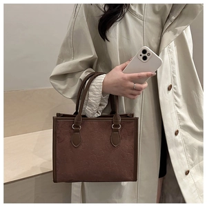Detail of dark brown tote bag featuring clover embossed pattern held by a model