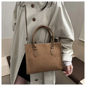 Brown embossed clover tote bag styled with a beige trench coat for a casual look