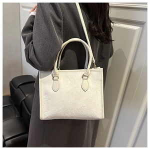 Detail of white tote bag with embossed clover patterns and cylindrical handle