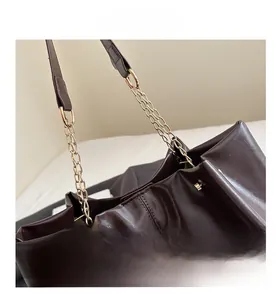 Macro shot of dark brown oil wax leather texture and gold chain strap of the tote bag