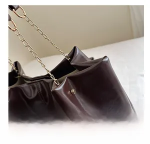 Detail of dark brown leather tote featuring shiny finish and gold chain straps