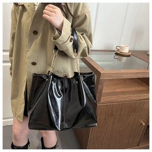 Detail of glossy black tote bag with metallic studs and chain strap on a trench coat