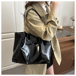 Glossy black patent leather tote bag with metal chain strap shown in a lifestyle setting