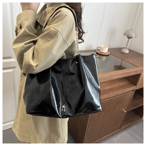 Detail of glossy black tote bag with gold chain strap worn by a model in a minimal room