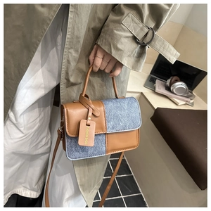 Detail of color-block tote featuring blue textured fabric and brown leather knot handle