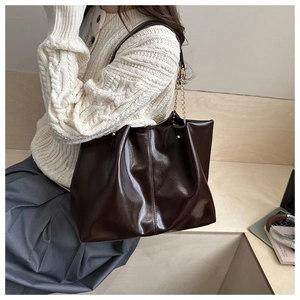 Close-up of a large coffee-brown tote bag with leather texture and gold chain straps