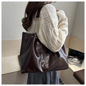 Detail of dark brown leather tote bag with chain strap shown on model shoulder