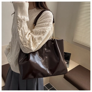 Detailed side view of dark brown tote bag with glossy finish and chain shoulder strap