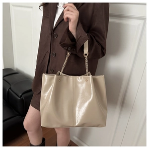 Detail of cream glossy patent leather tote bag featuring gold studs and chain strap